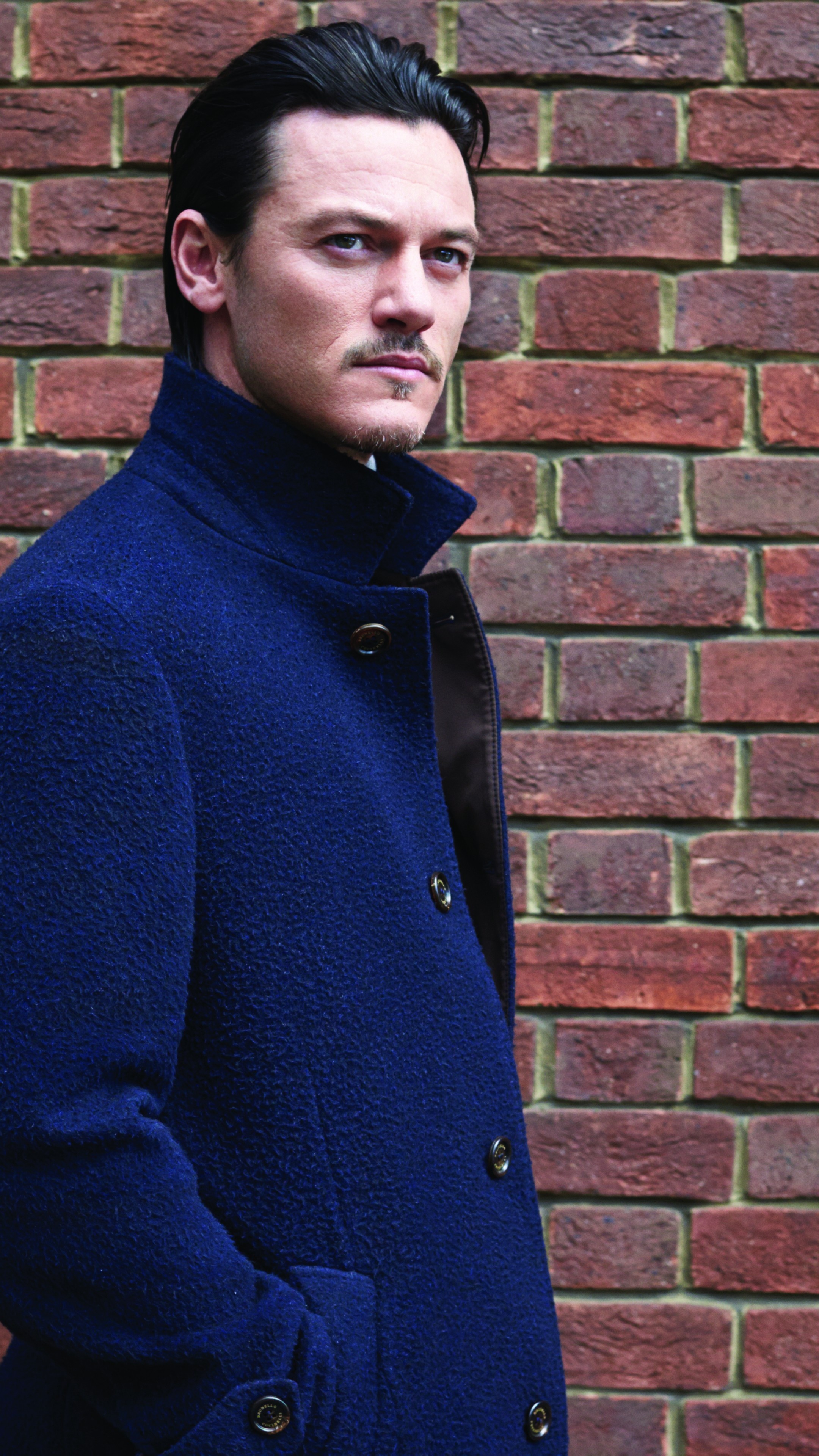 Luke Evans wallpaper, Blue cloak fashion, Brick wall backdrop, Striking celebrity look, 2160x3840 4K Phone