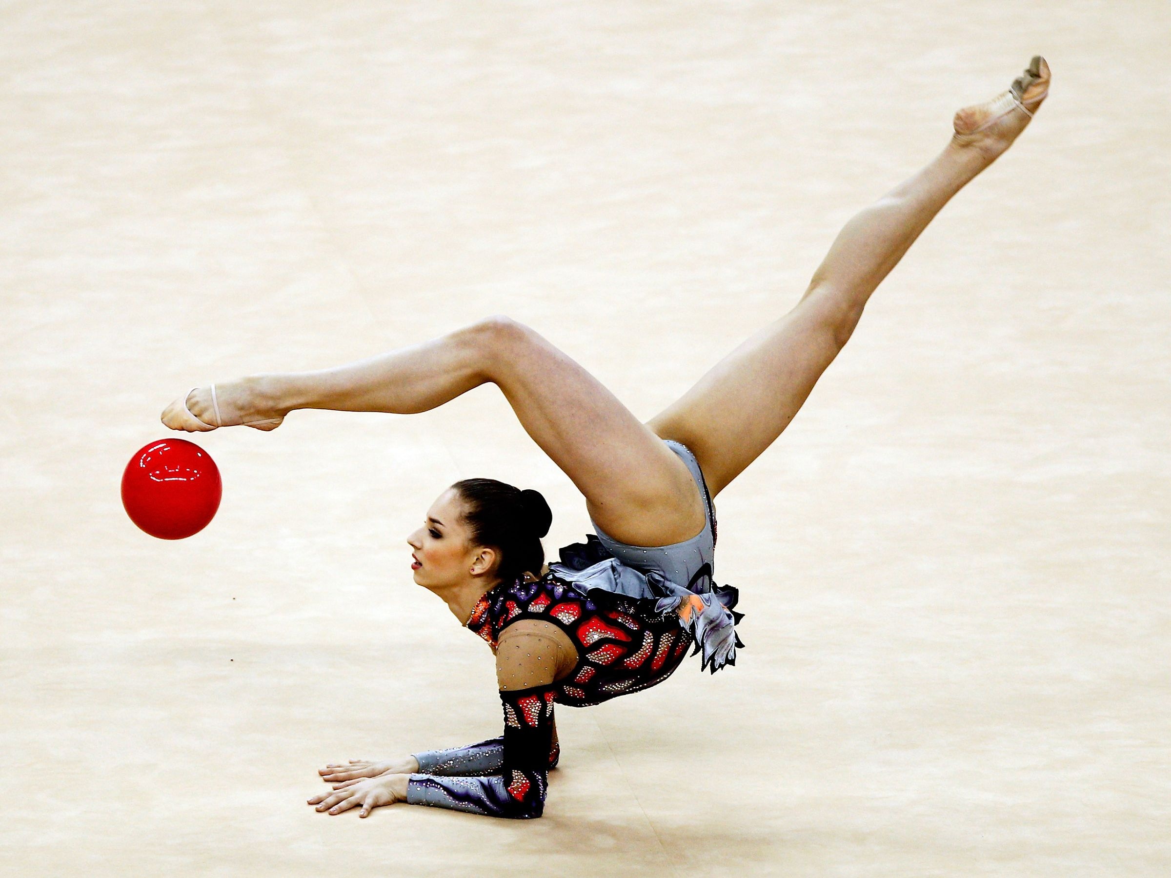 Rhythmic Gymnastics: A female gymnast performs a stretch with a red ball, Competitive artistic sport. 2400x1800 HD Wallpaper.