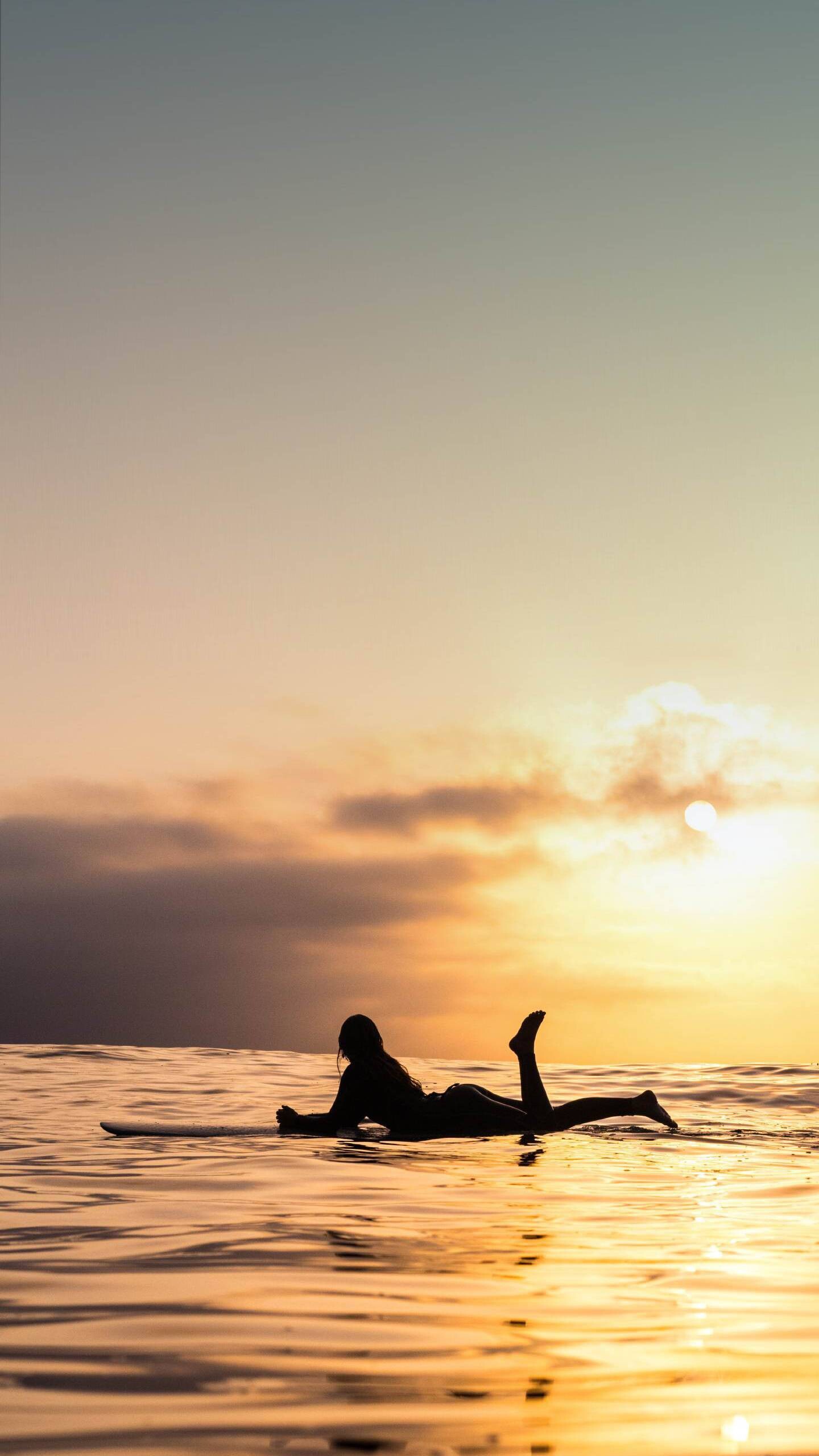 Girl Surfing: Outdoor vacation activity, Woman relaxing on a surfboard at sunset. 1440x2560 HD Background.