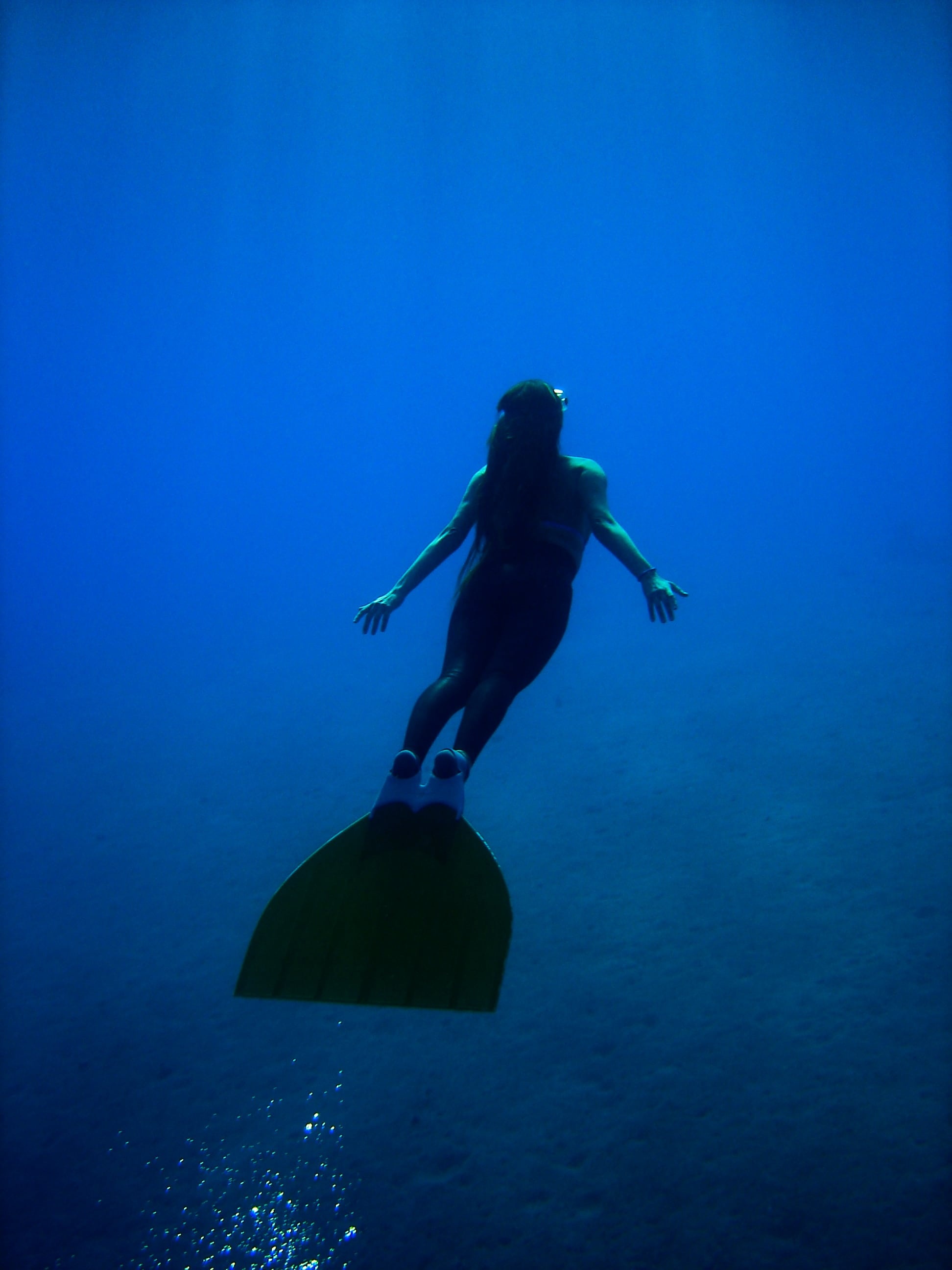 Freediving: Skin diver equipped with a monofin explores the sea depth. 1950x2600 HD Background.