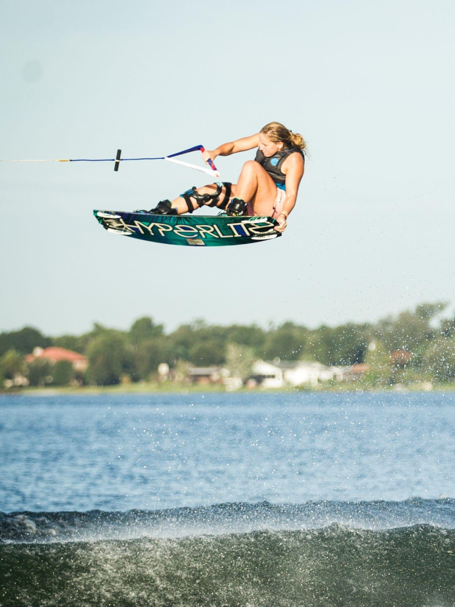 Wakeboarding: Girl uses a short surfboard with foot bindings to perform a tail grab trick. 1540x2050 HD Wallpaper.