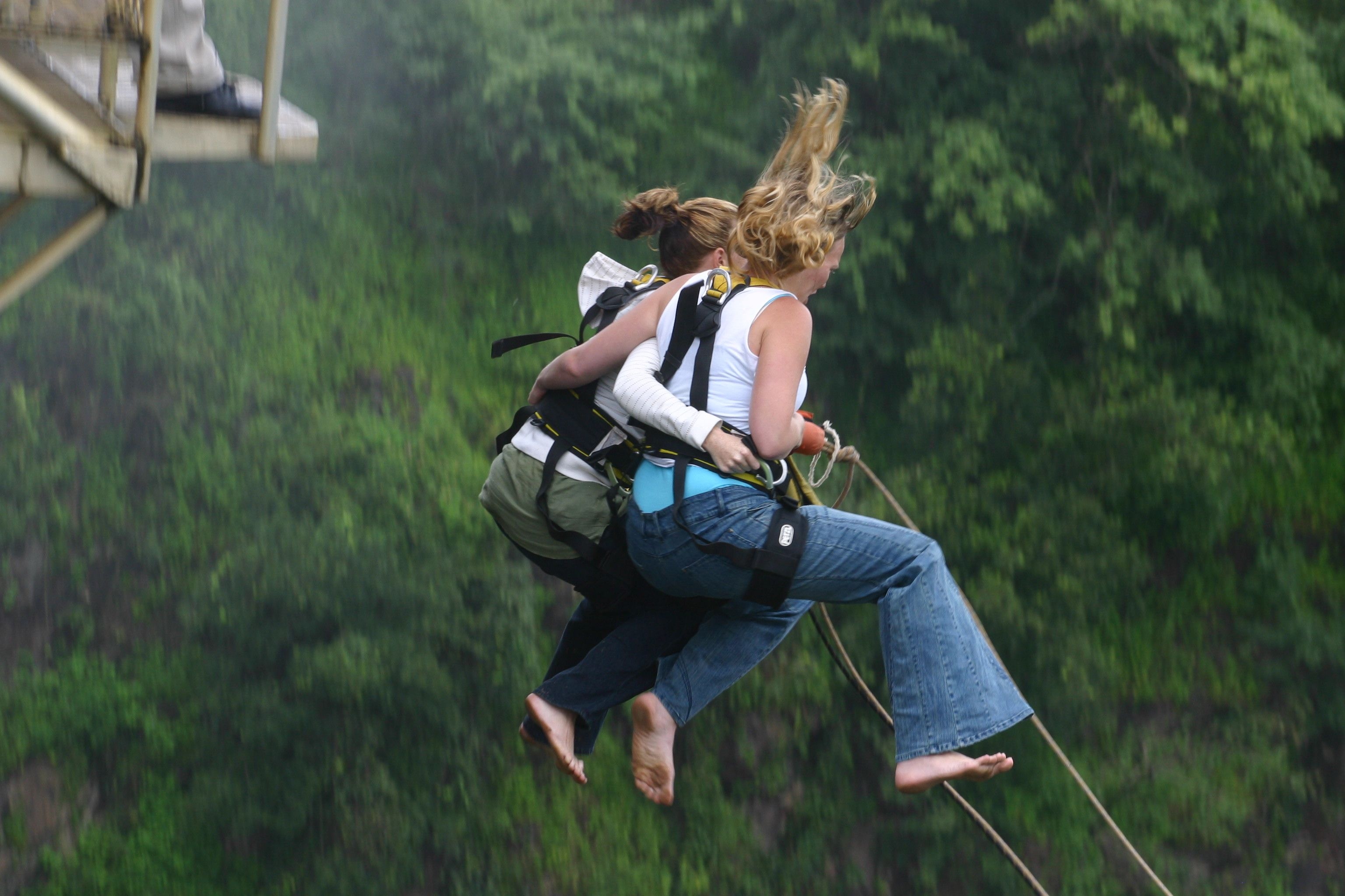Bungee Jumping: A couple of girls is connected to an elastic cord while falling from a mountain base. 3080x2050 HD Background.