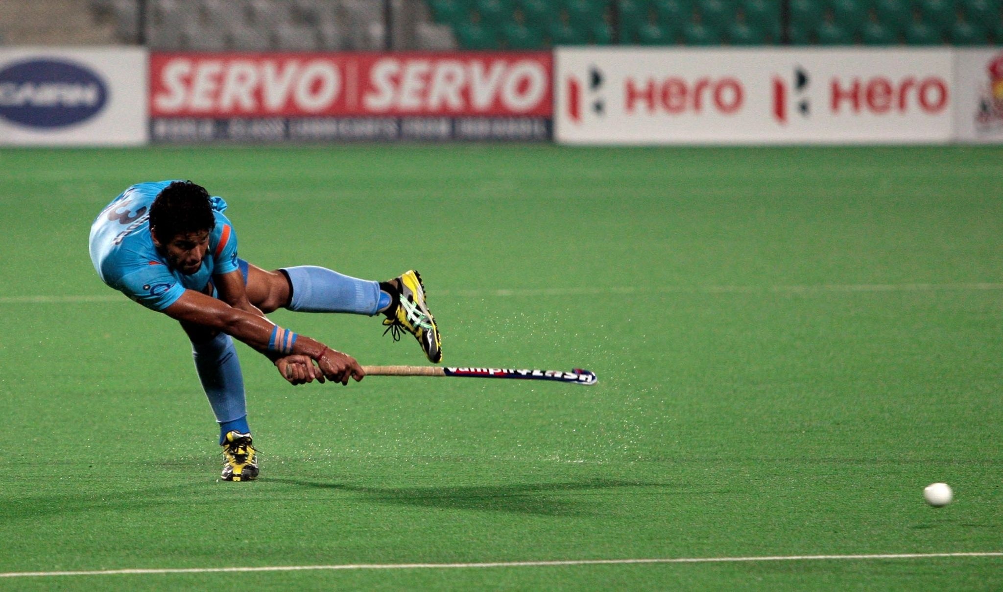 Field Hockey: Rupinder Pal Singh of the Indian team bends over while striking the ball with a stick. 2050x1210 HD Background.