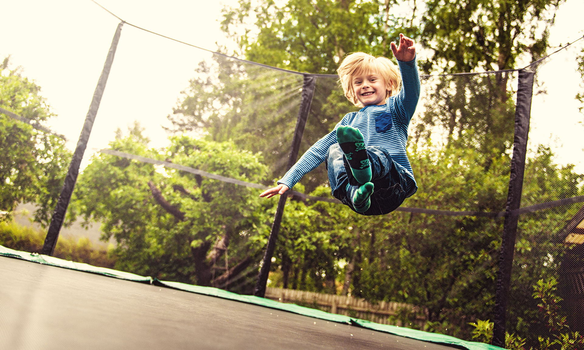 Trampolining: A happy boy jumps on a backyard trampoline, Recreational outdoor activity and sport. 1920x1160 HD Background.