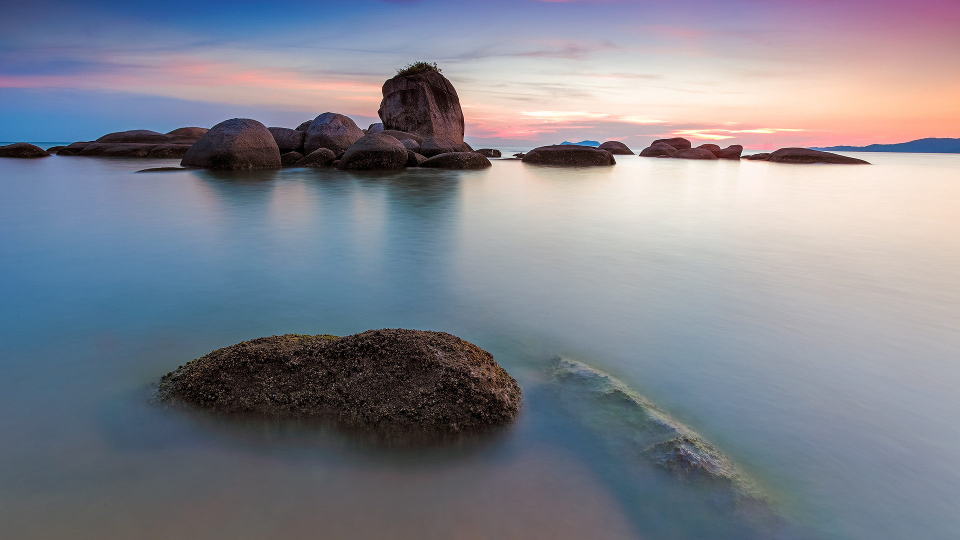 Seascape: Mysterious foggy still water surface at the rocky coast of the sea, Sunset time. 1920x1080 Full HD Wallpaper.