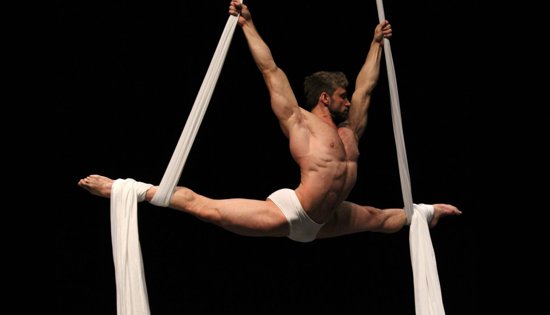 Aerial Silks: A professional male aerialist performs a stretch while hanging from a white fabric. 1920x1100 HD Wallpaper.