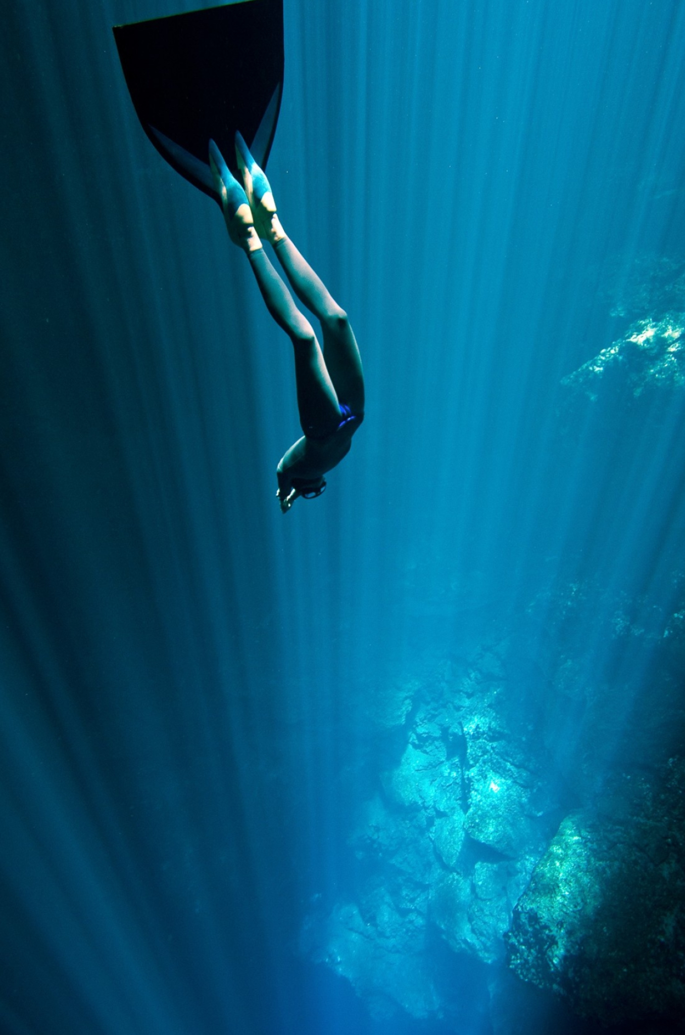 Freediving: A diver equipped with a monofin moves deeper to the bottom. 1360x2050 HD Background.