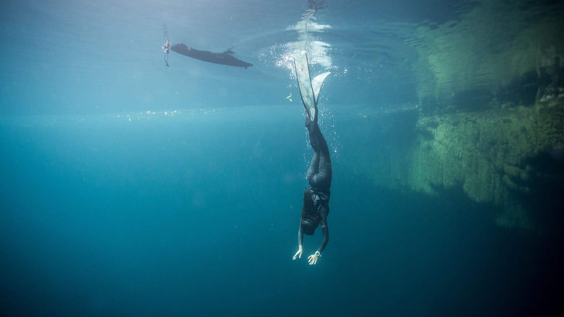 Freediving: A female skin underwater swimmer dives deeply into the lake. 1920x1080 Full HD Wallpaper.