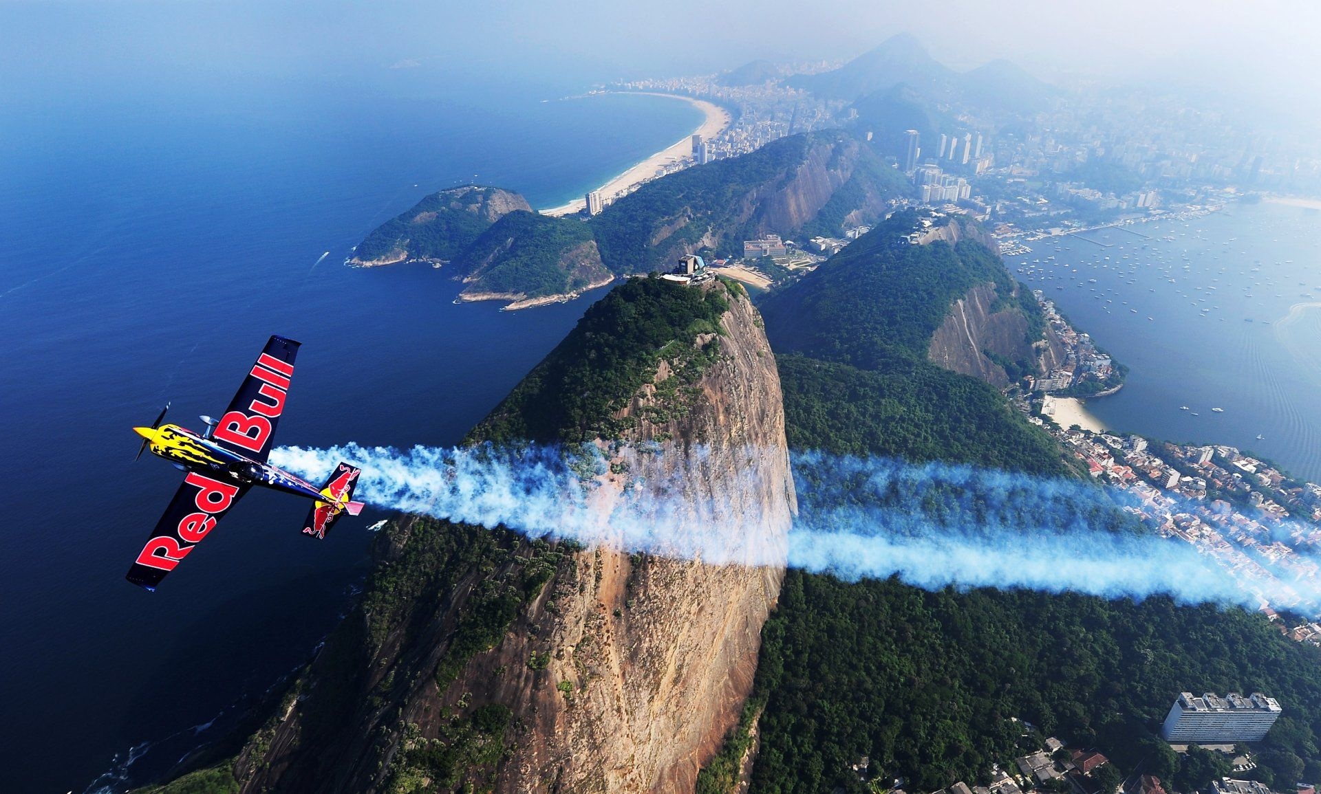 Air Sports: Red Bull monoplane competes in an air race around Rio de Janeiro, vapor trail over the Sugarloaf, Pao de Acucar mountain, Red Bull Air Race. 1920x1160 HD Background.