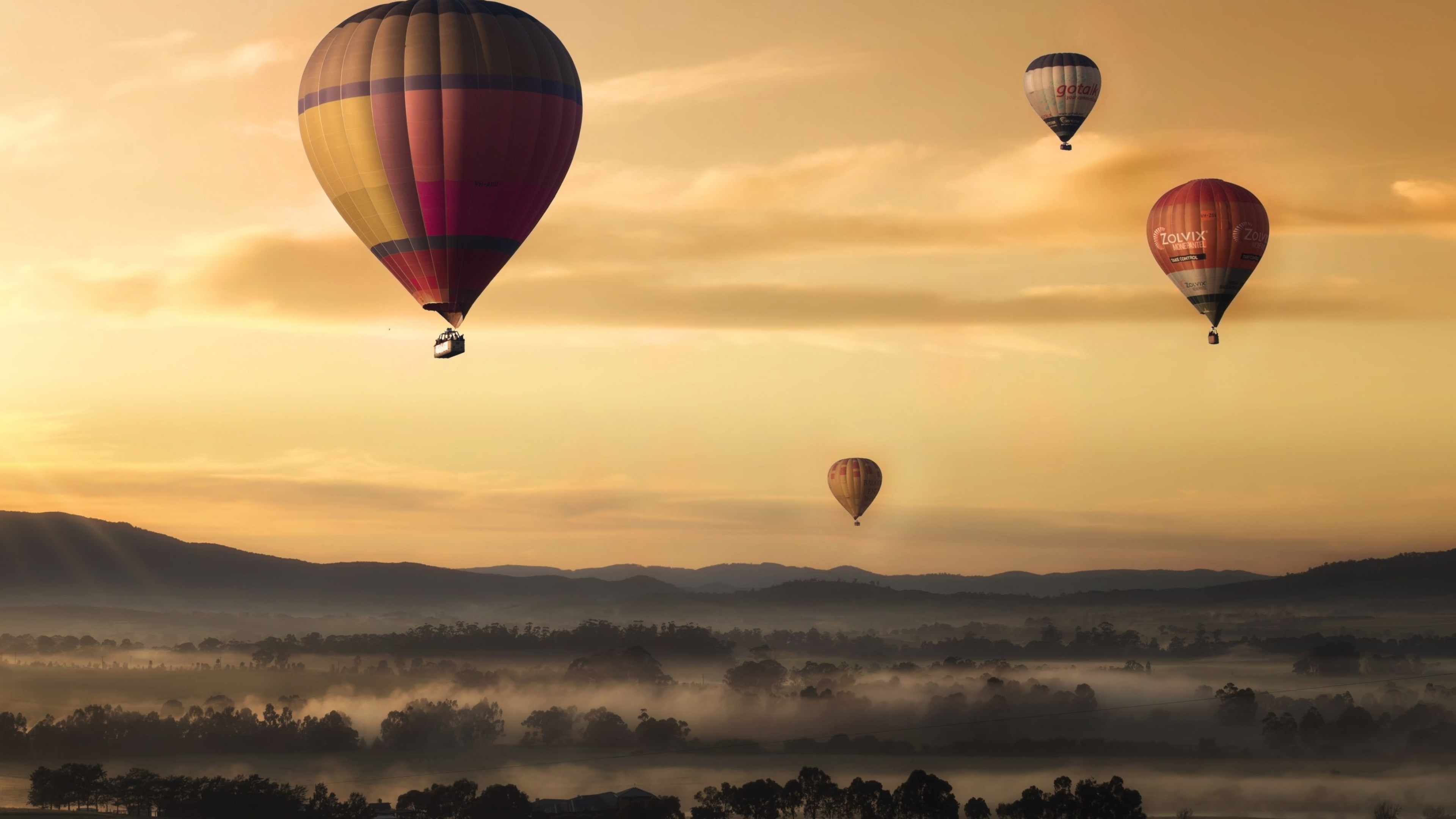 Air Sports: Hot-air balloons fill the sunset sky on a foggy and cloudy evening. 3840x2160 4K Background.